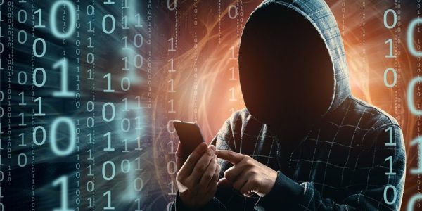 A young hacker in a hood hacks a smartphone, a hacker attack, a silhouette of a man, mixed media. The concept of a sudden attack, cryptography, data security, mobile Internet.