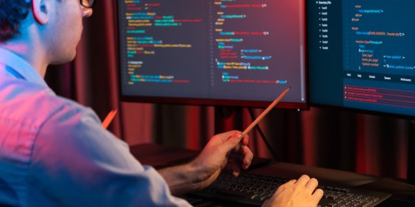 Working IT developer pointing with pencil on online software development coding database application on pc screens, creating program for firmware on website at neon light modern office home. Gusher.