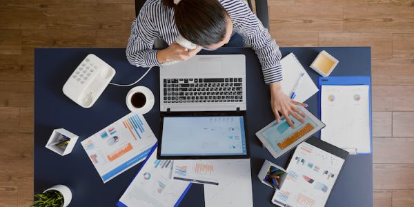 Top view of businesswoman discussing with manager explaining company statistics using landline while analyzing management strategy papaerwork. Accountant sittinga t desk in business startup office
