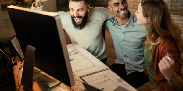 Young start-up team celebrating business success while using computer in the office.